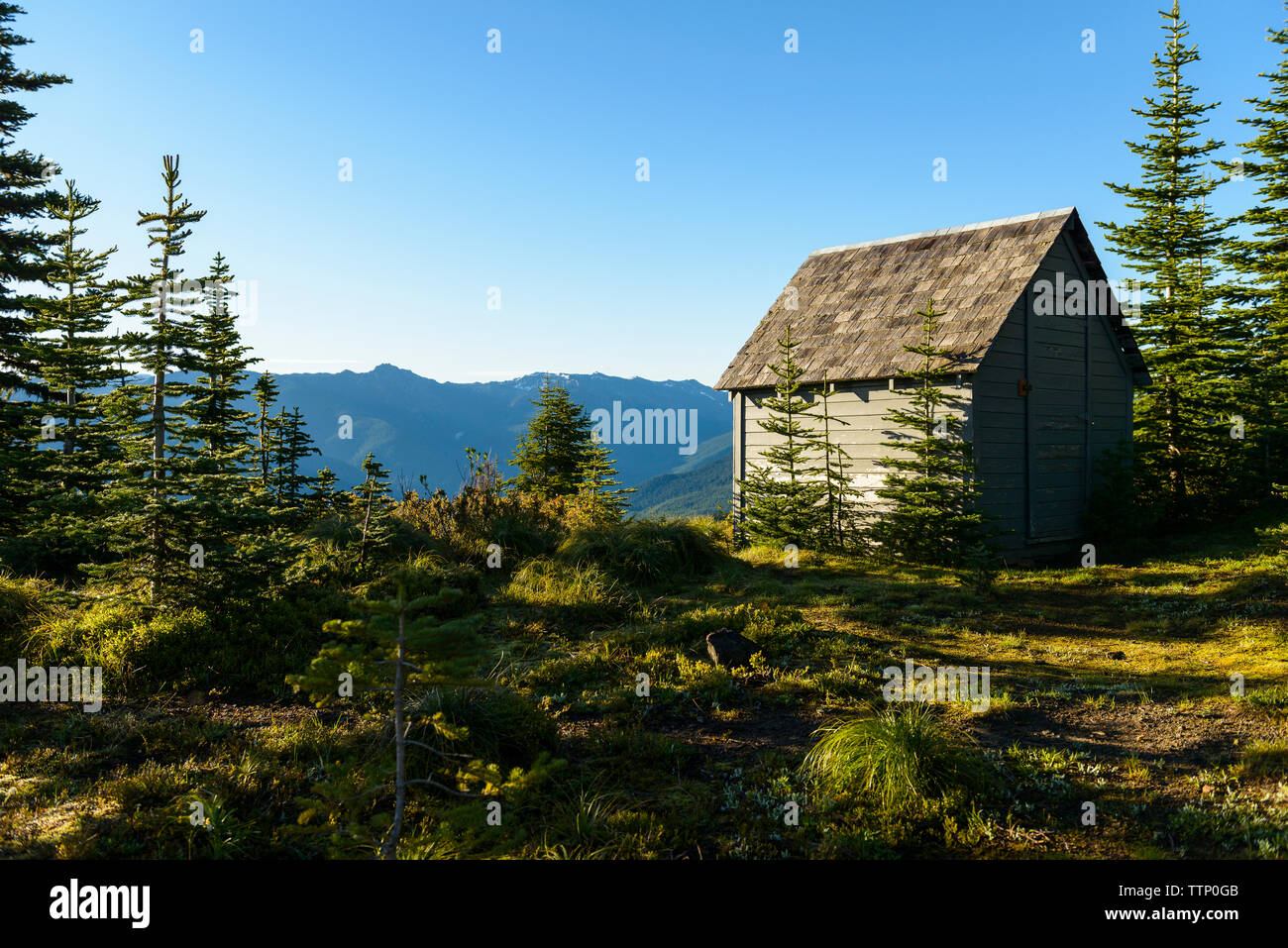 Log Cabin On Field Against Mountains And Clear Sky Stock Photo