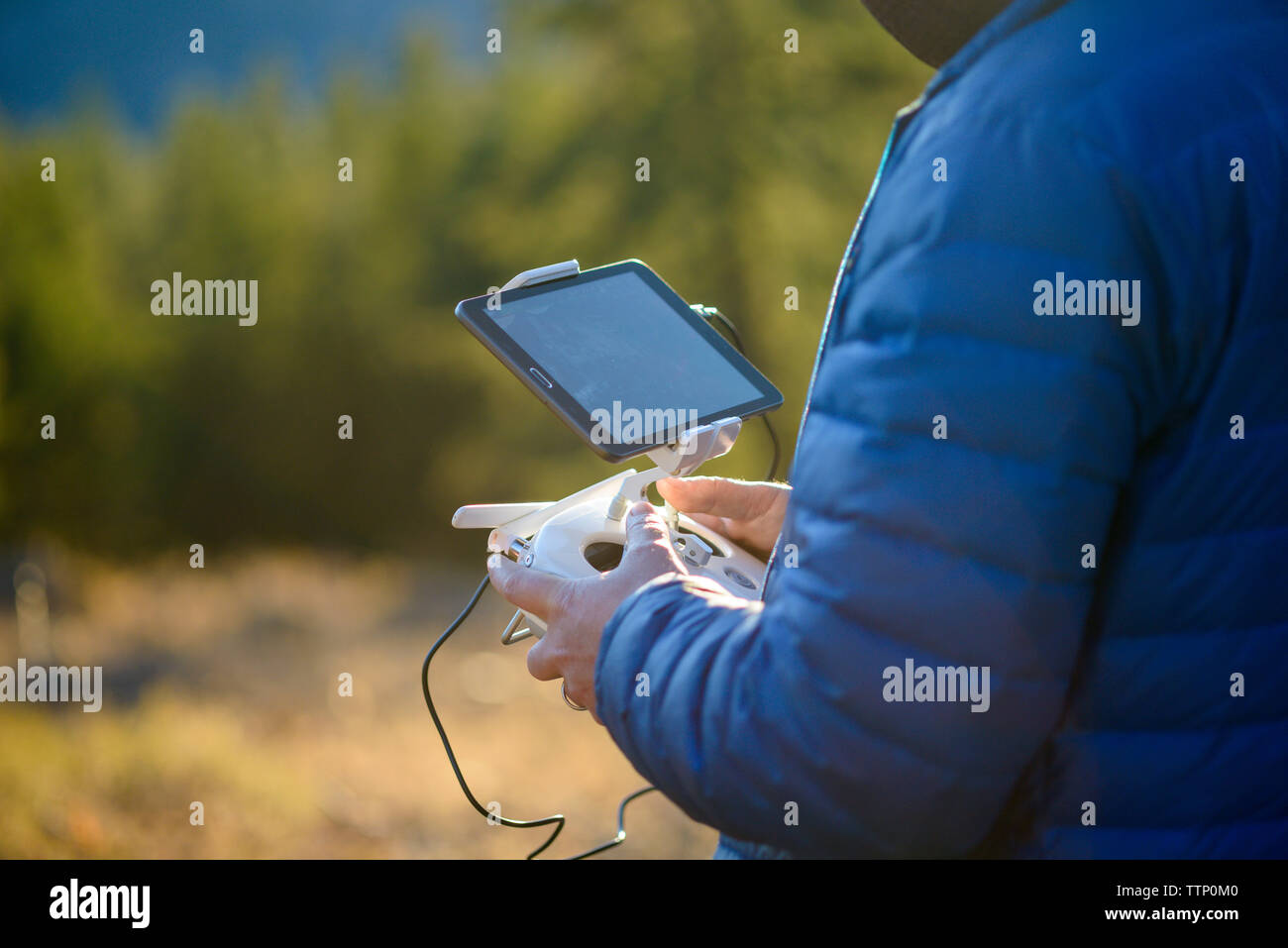 Midsection of man operating drone with tablet computer and remote control while standing in forest Stock Photo