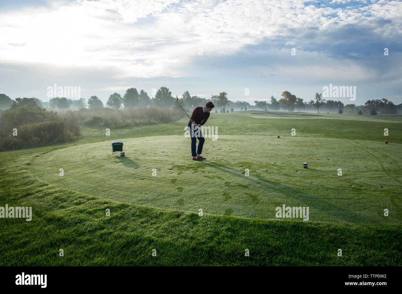 Man playing golf on field against sky on sunny day Stock Photo