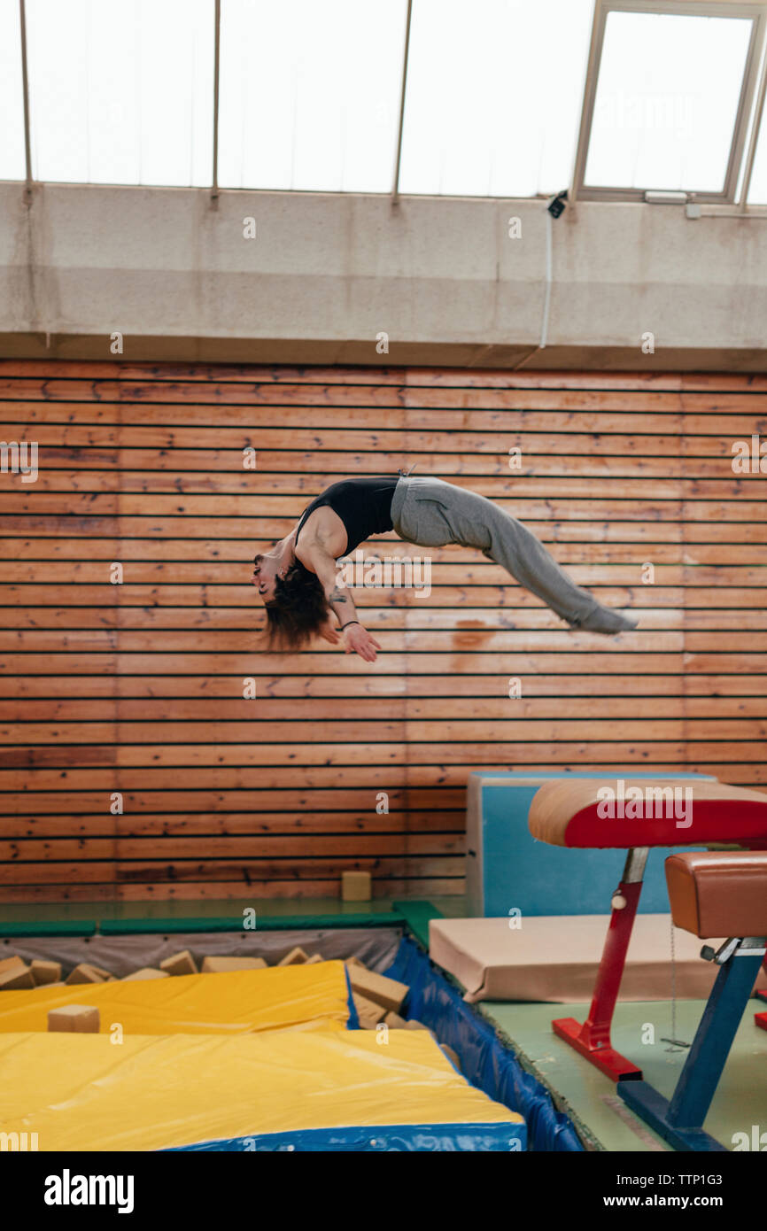 Side view of gymnast jumping from gymnastics equipment at gym Stock