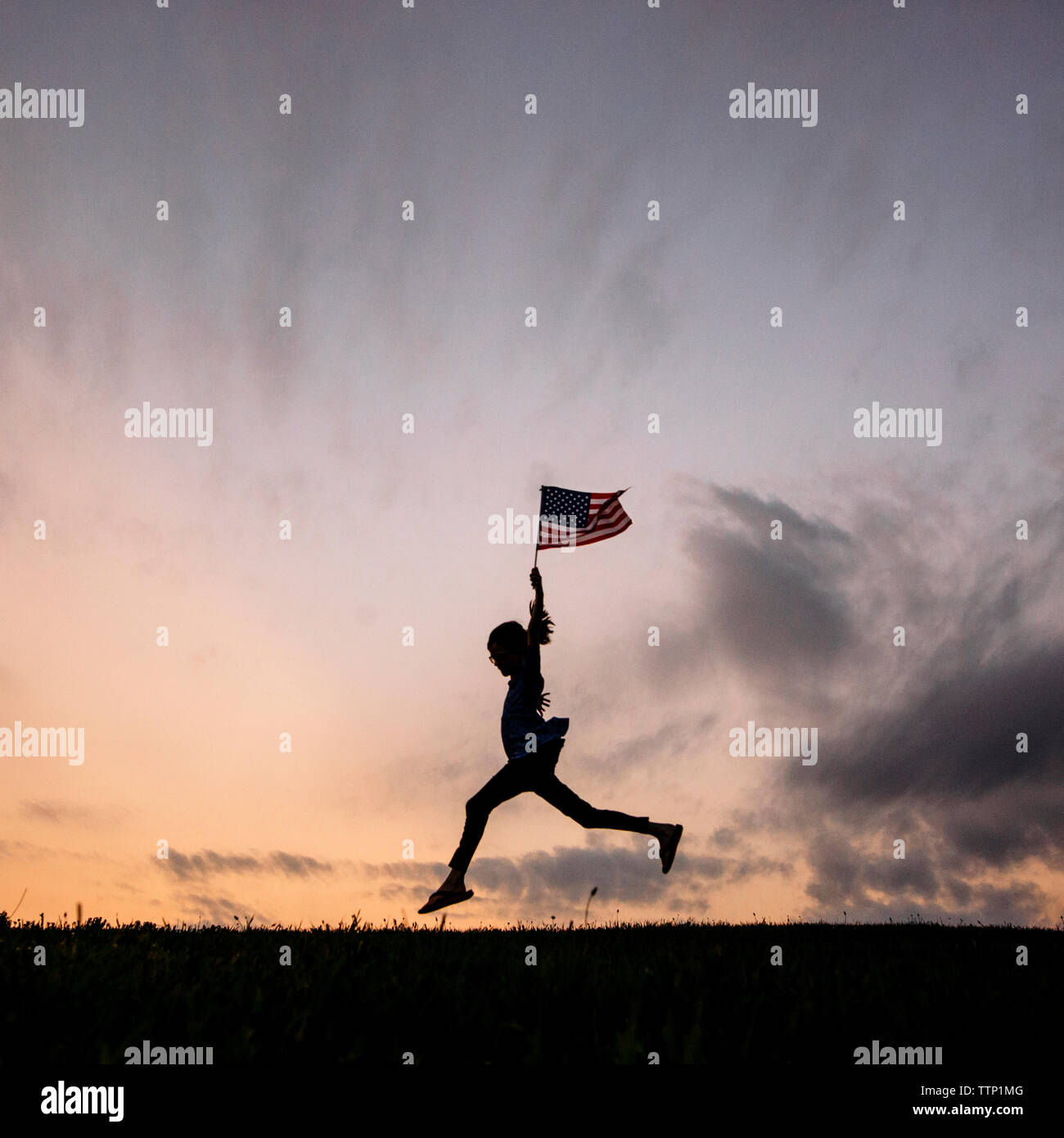 Silhouette girl with American flag running on field against sky Stock Photo