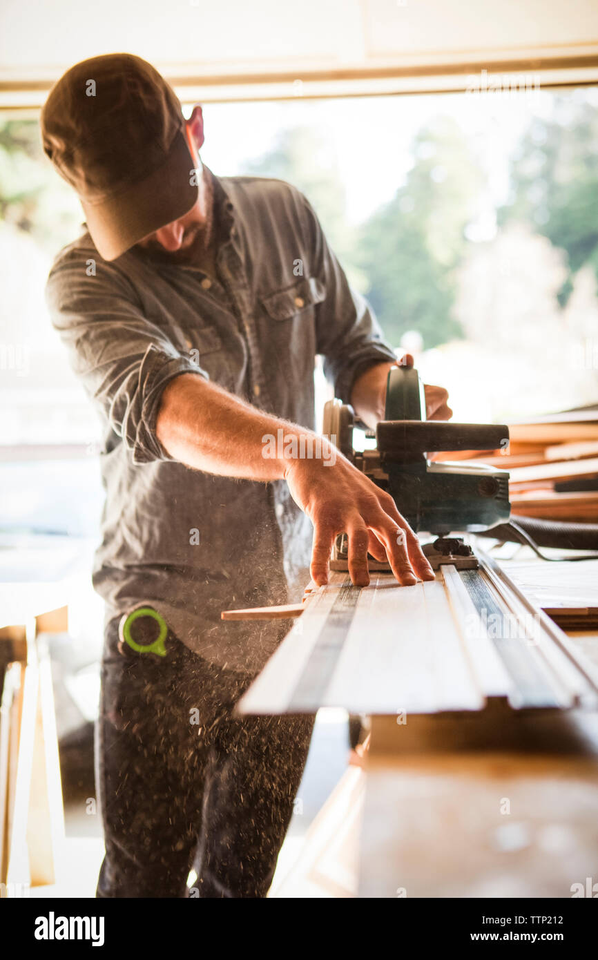 Artist using circular saw on wooden plank at workbench in