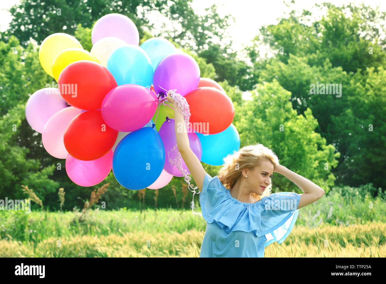 Happy Woman With Colorful Balloons In Field On Blue Sky Background happy-woman-with-colorful-balloons-in-field-on-blue-sky-background