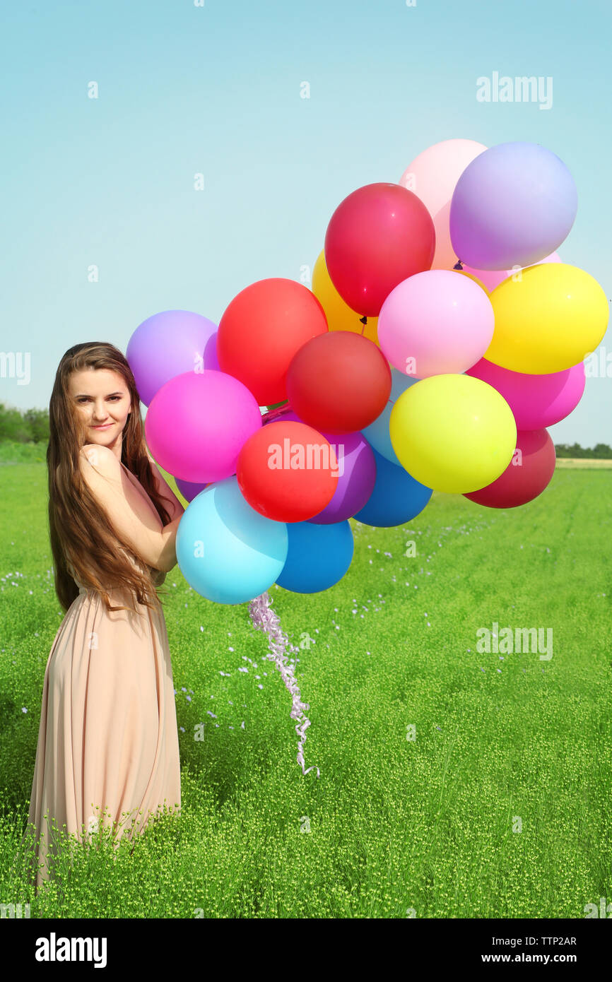 Happy Woman With Colorful Balloons In Field On Blue Sky Background happy-woman-with-colorful-balloons-in-field-on-blue-sky-background