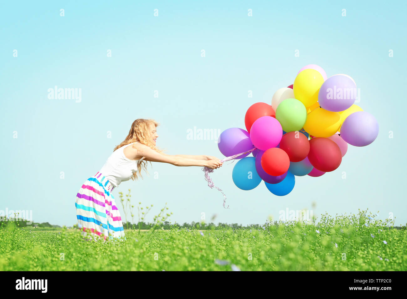 Happy Woman With Colorful Balloons In Field On Blue Sky Background happy-woman-with-colorful-balloons-in-field-on-blue-sky-background