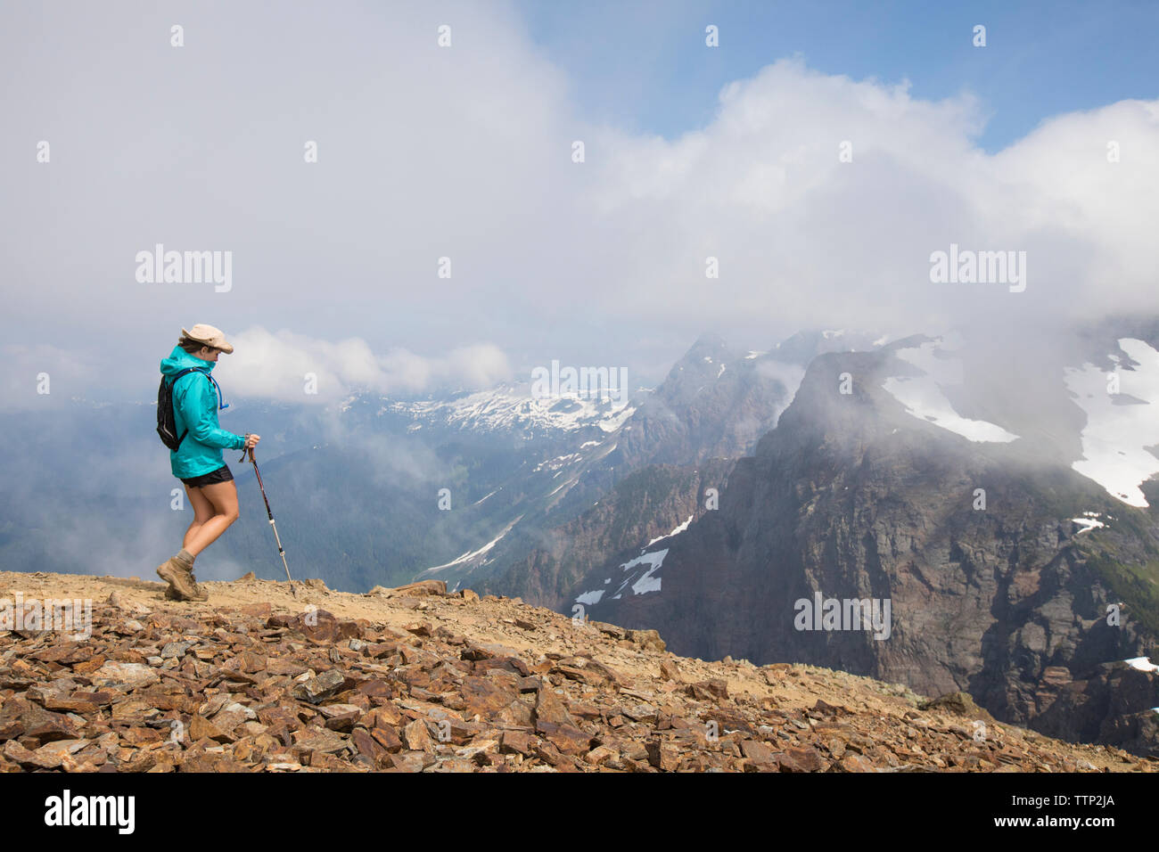 Side view of female hiker with hiking pole walking on mountain against cloudy sky Stock Photo