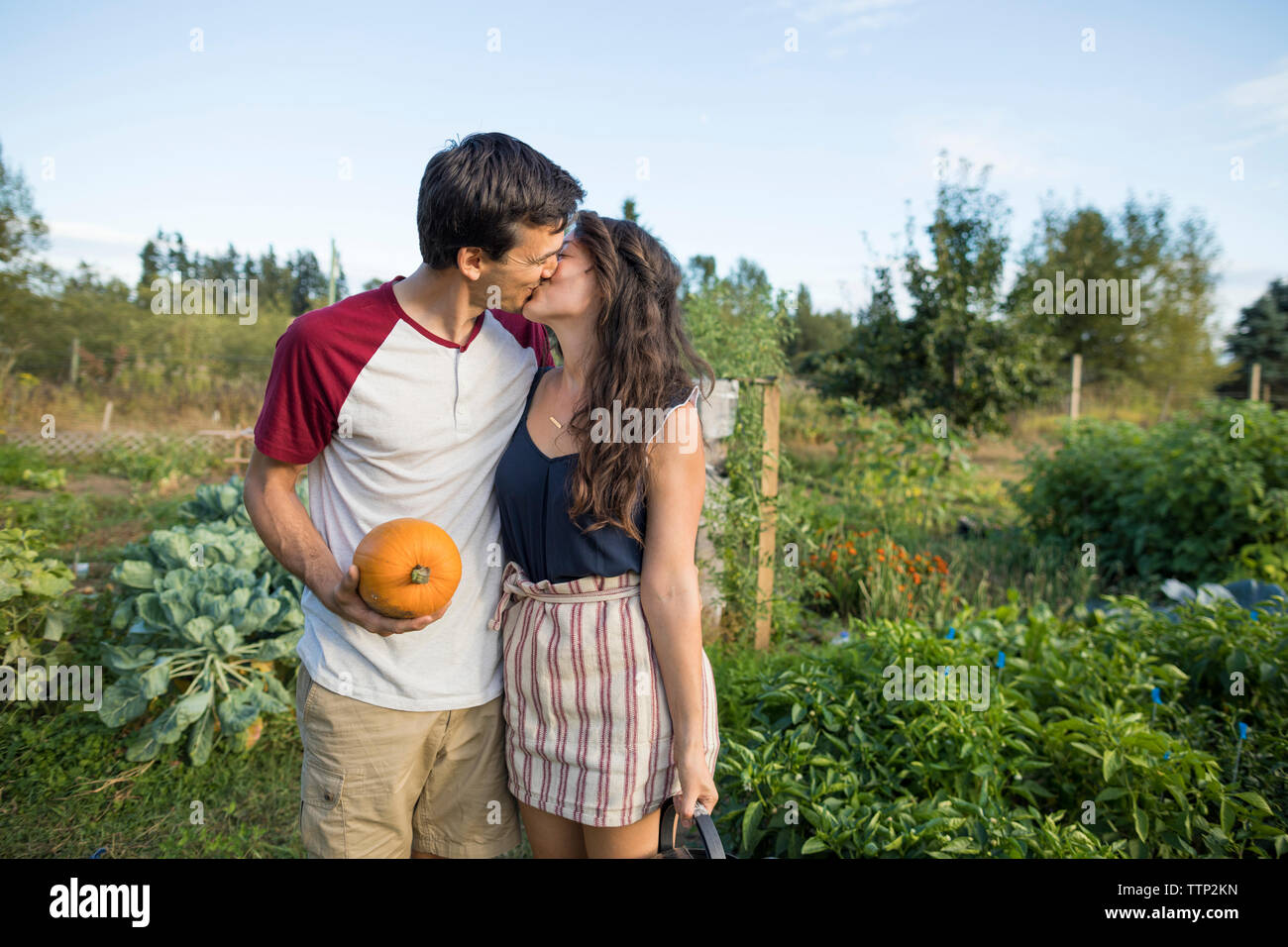 Young couple kissing while standing against sky at community garden Stock Photo