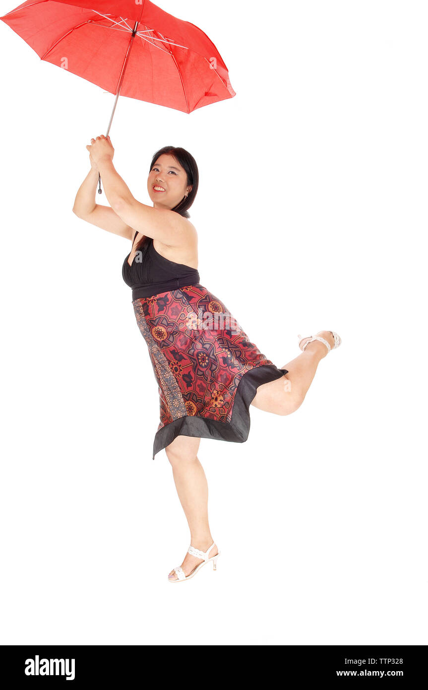 A gorgeous young Asian woman in a dress and heels flying away with a red umbrella, lifting one leg, isolated for white background Stock Photo