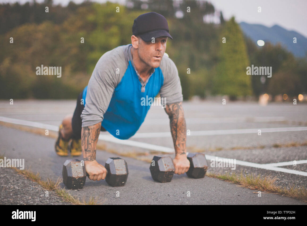 Man with dumbbells doing push-ups on road at park Stock Photo
