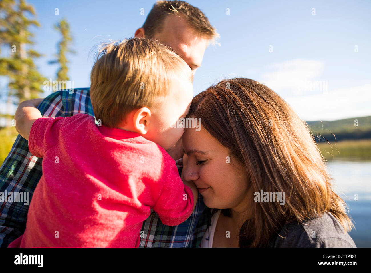 Loving son touching mother's head while being carried by father against lake Stock Photo