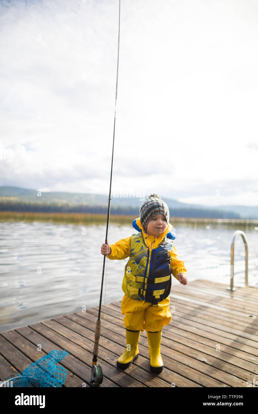 Baby boy wearing raincoat and life jacket while holding fishing