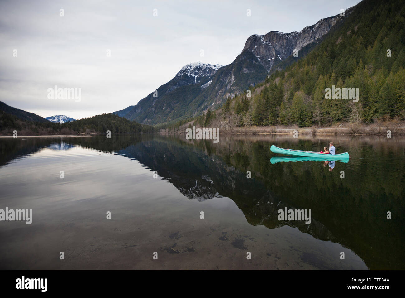 Mid distance view of young couple canoeing on lake against mountains Stock Photo