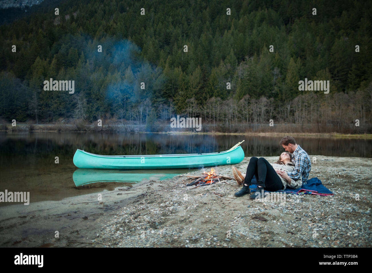 Full length of couple resting by campfire on lakeshore at Silver Lake Provincial Park Stock Photo