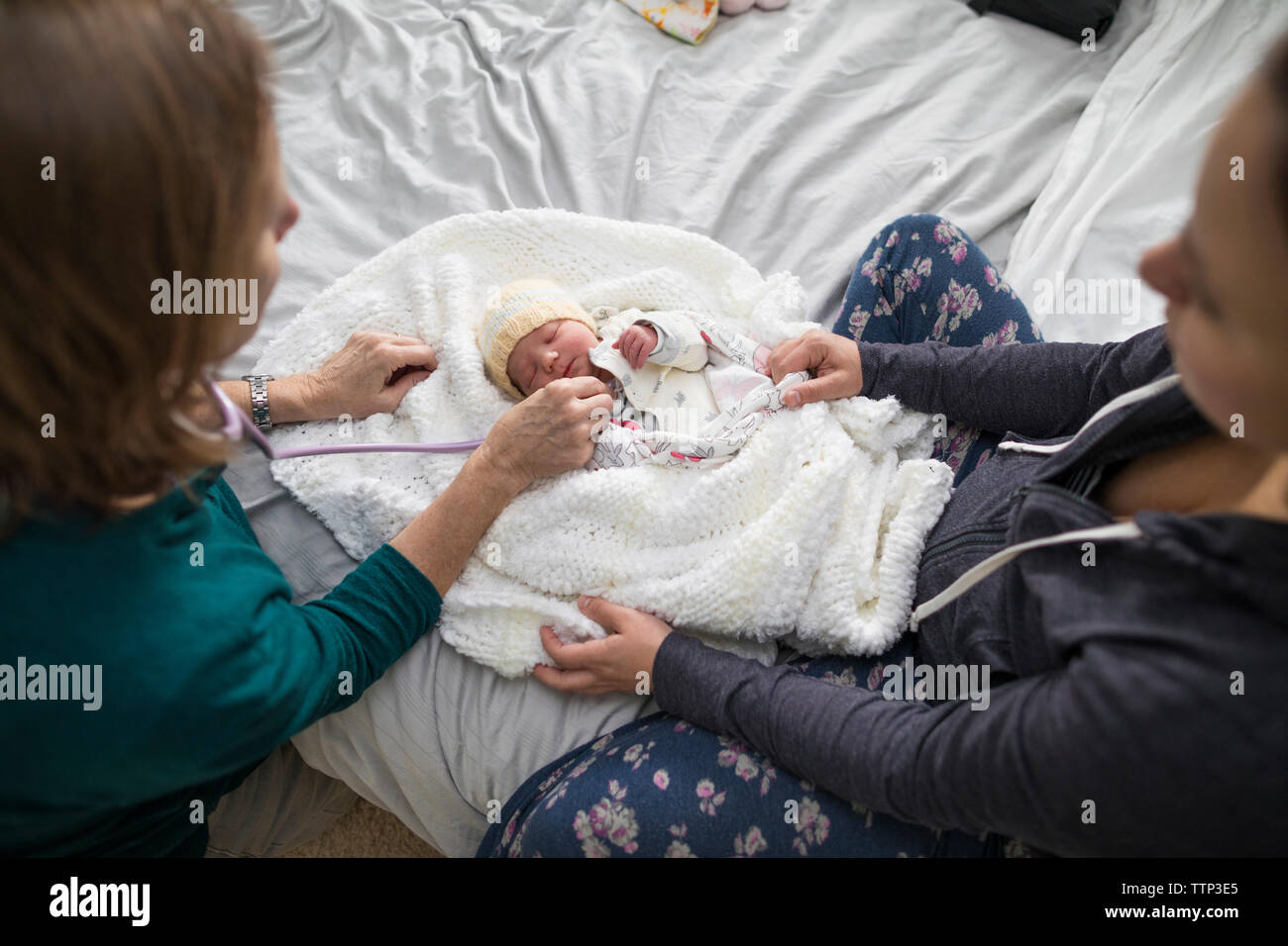 High angle view of midwife examining newborn baby girl while mother sitting on bed at home Stock Photo