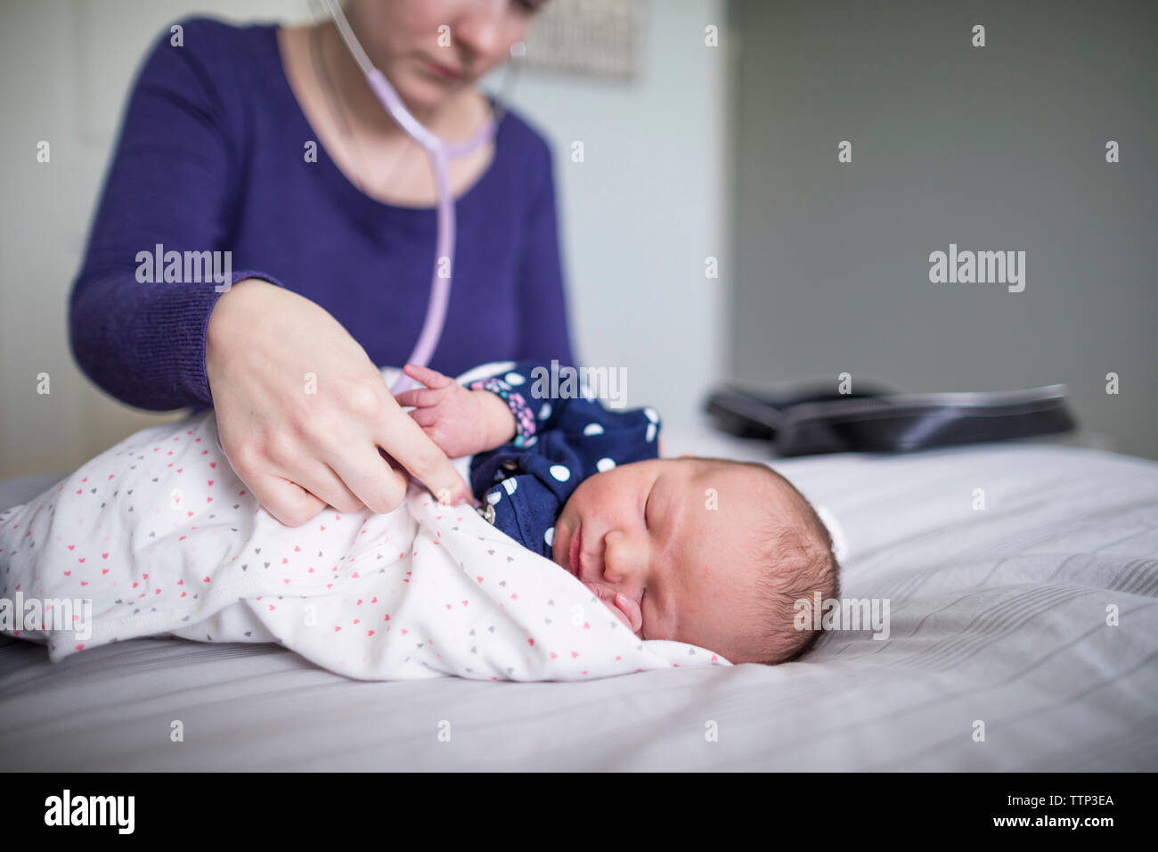 Midwife examining newborn sleeping baby girl with stethoscope on bed at home Stock Photo