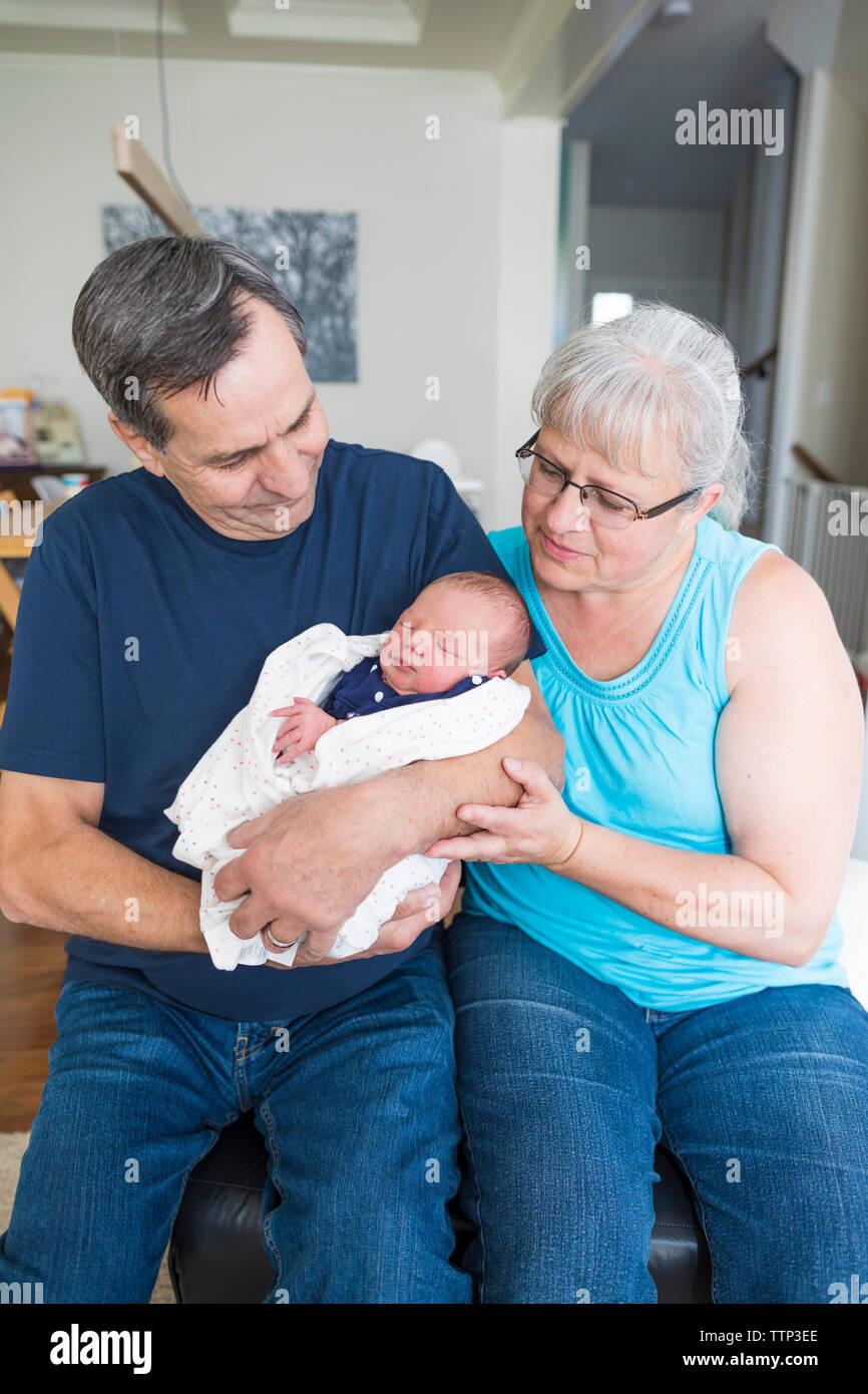 Grandparents with cute newborn granddaughter sitting at home Stock Photo