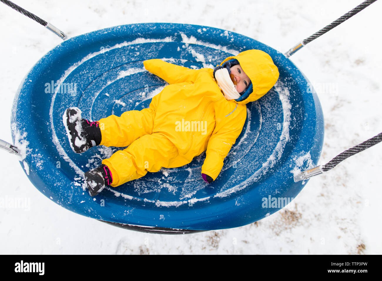 Toddler laying on large swing during winter visit to the park. Stock Photo