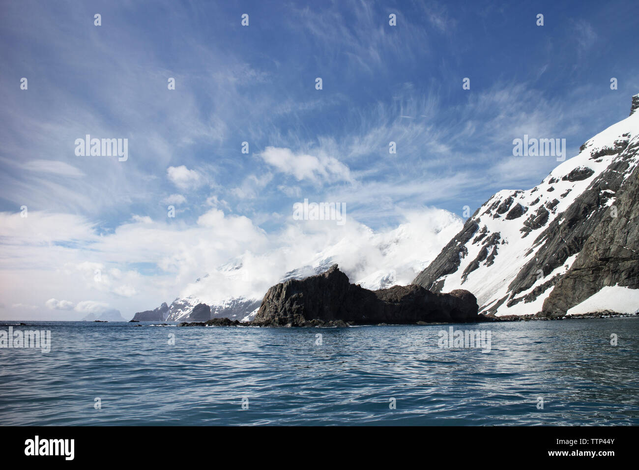 Sea and snow covered mountains against cloudy sky Stock Photo