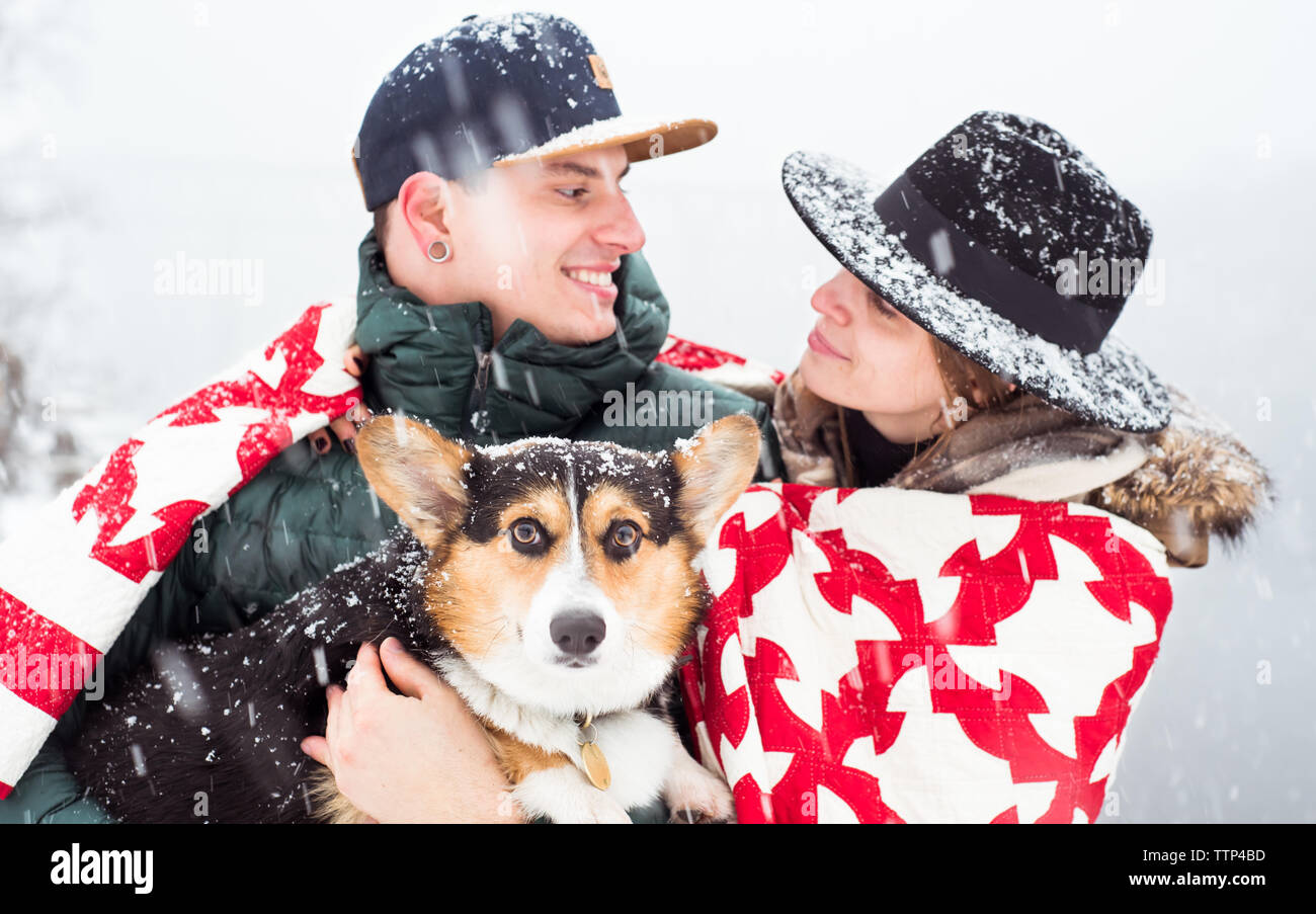 Young couple huddled in blanket holding dog and locking eyes Stock