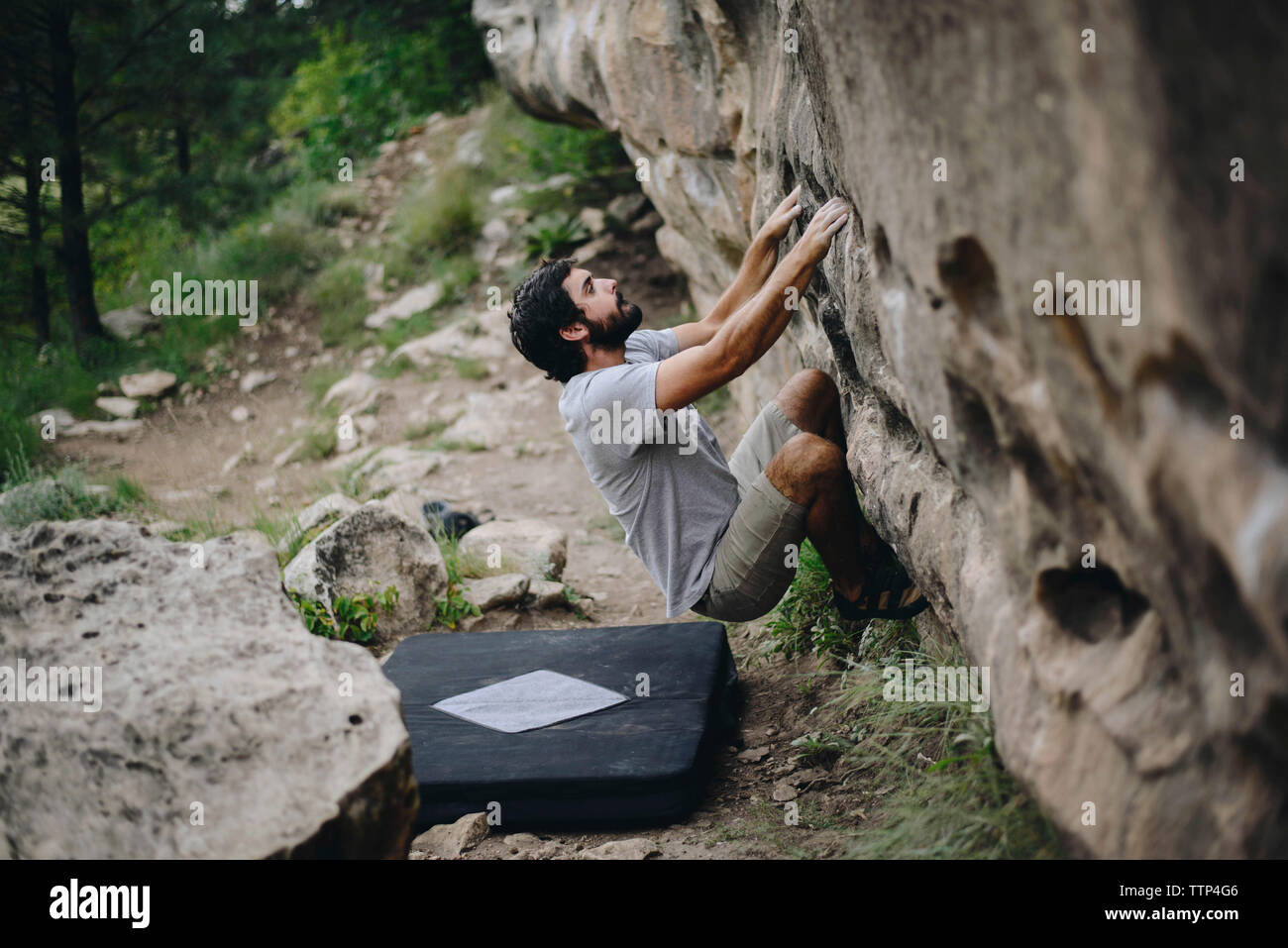 Man climbing rock by bouldering mat on field at forest Stock Photo Alamy