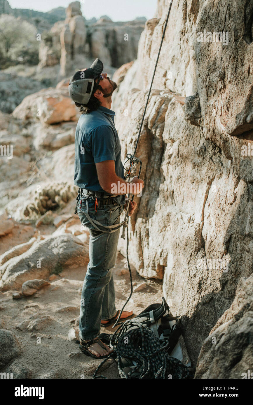 Hiker looking up while holding climbing rope by rock formation Stock Photo