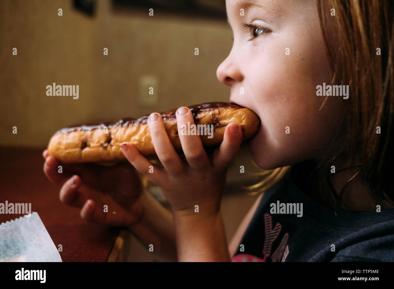 Side view of cute girl eating sweet food while sitting at home Stock Photo