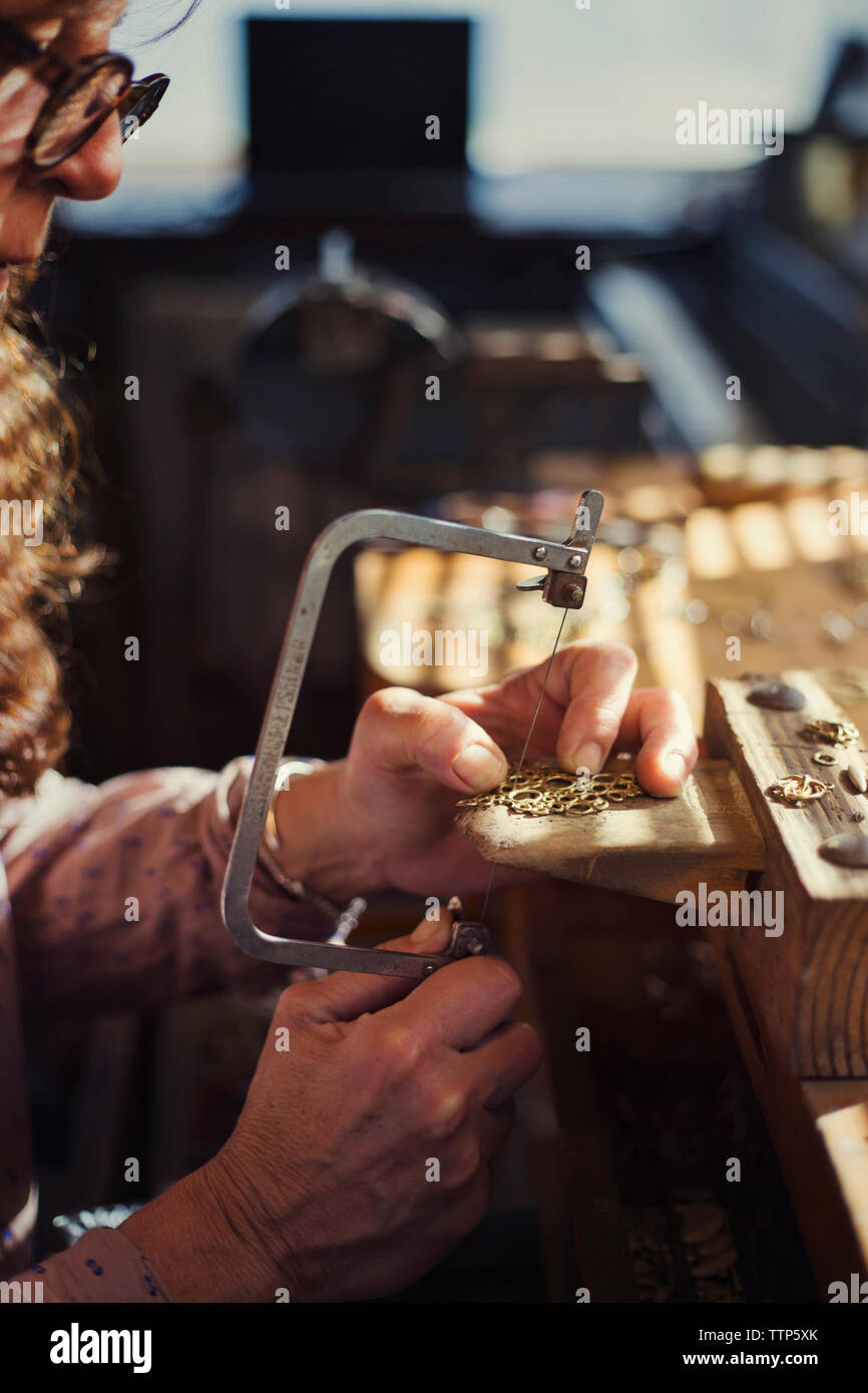 Cropped image of female goldsmith using saw while making jewelry in workshop Stock Photo