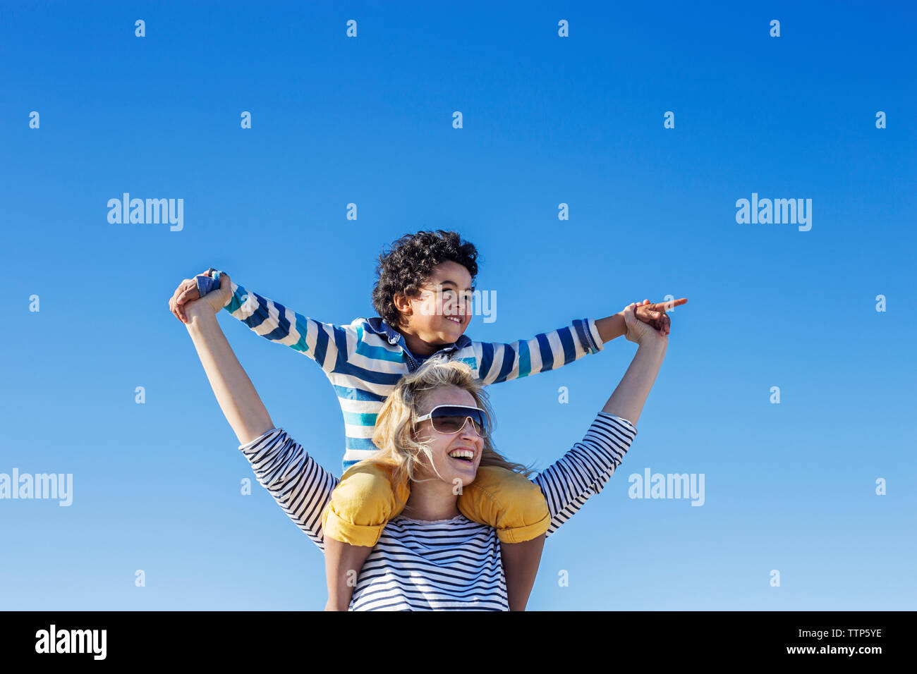 Low angle view of mother carrying son on shoulders against clear blue sky Stock Photo