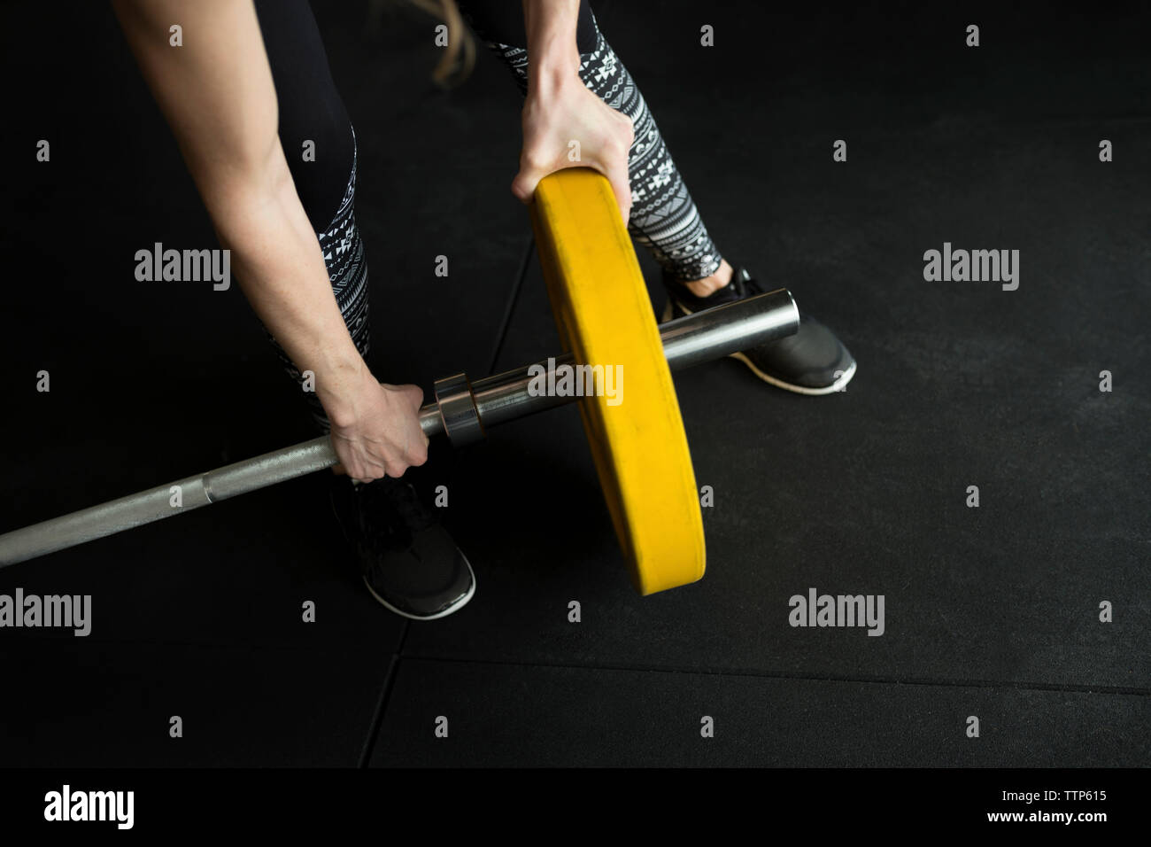 Low section of woman adjusting weight on barbell while exercising in gym Stock Photo