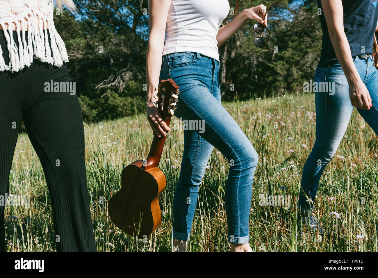 Woman carrying guitar walking with friends on grassy field Stock Photo