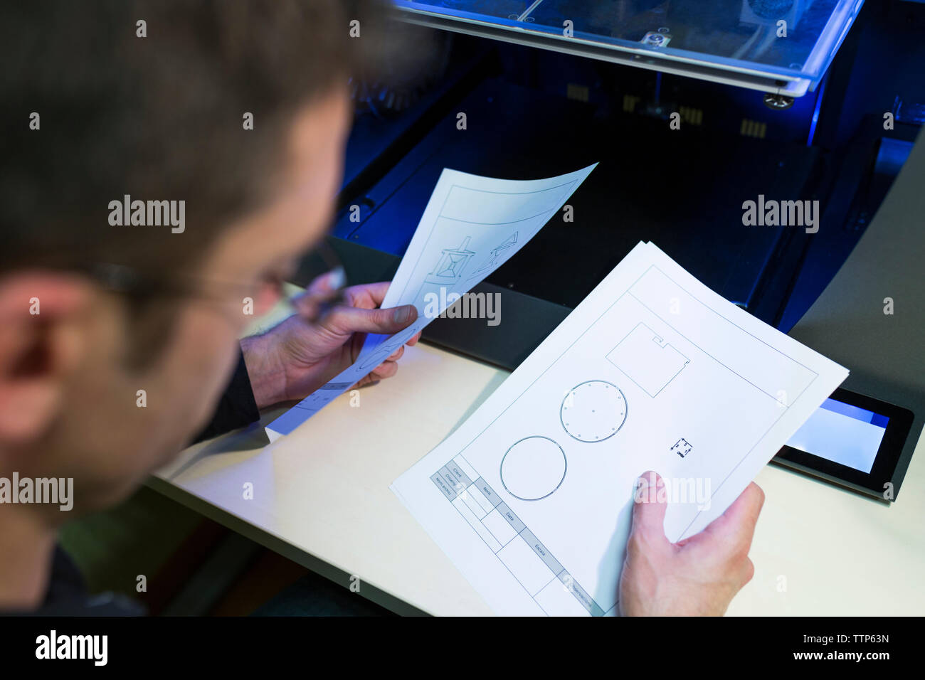 Engineer holding documents by 3D printer at table in office Stock Photo