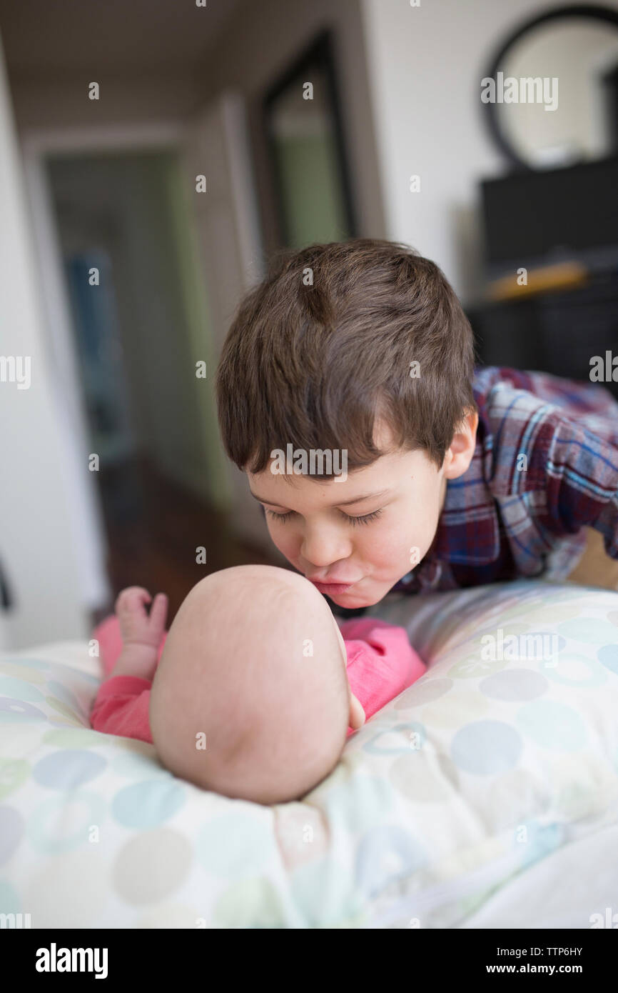 Brother kissing baby girl lying on bed at home Stock Photo