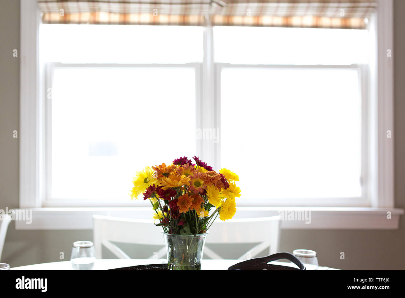 Flowers in vase against window on table at home Stock Photo