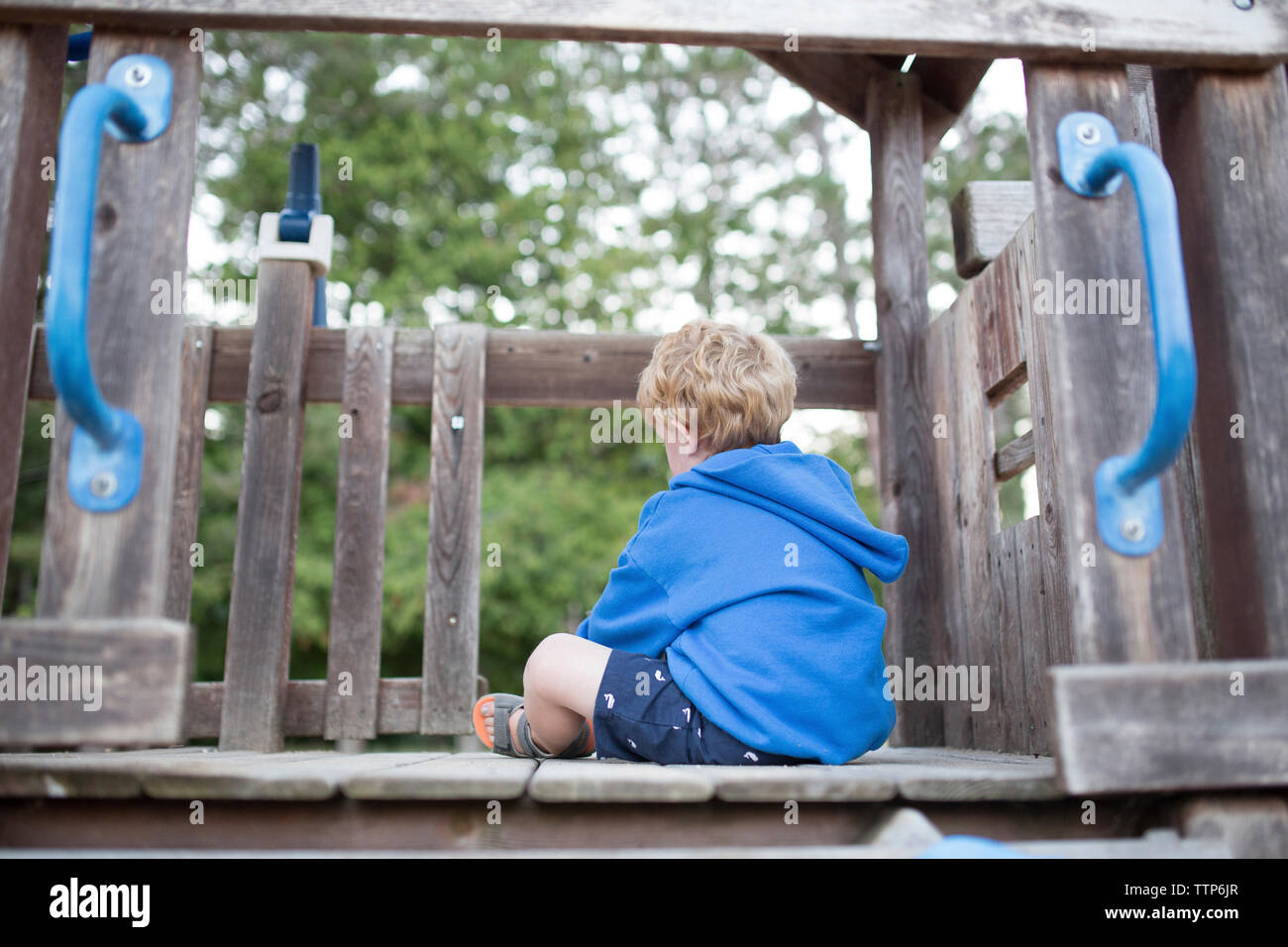 Rear view of boy sitting on wooden jungle gym at playground Stock Photo