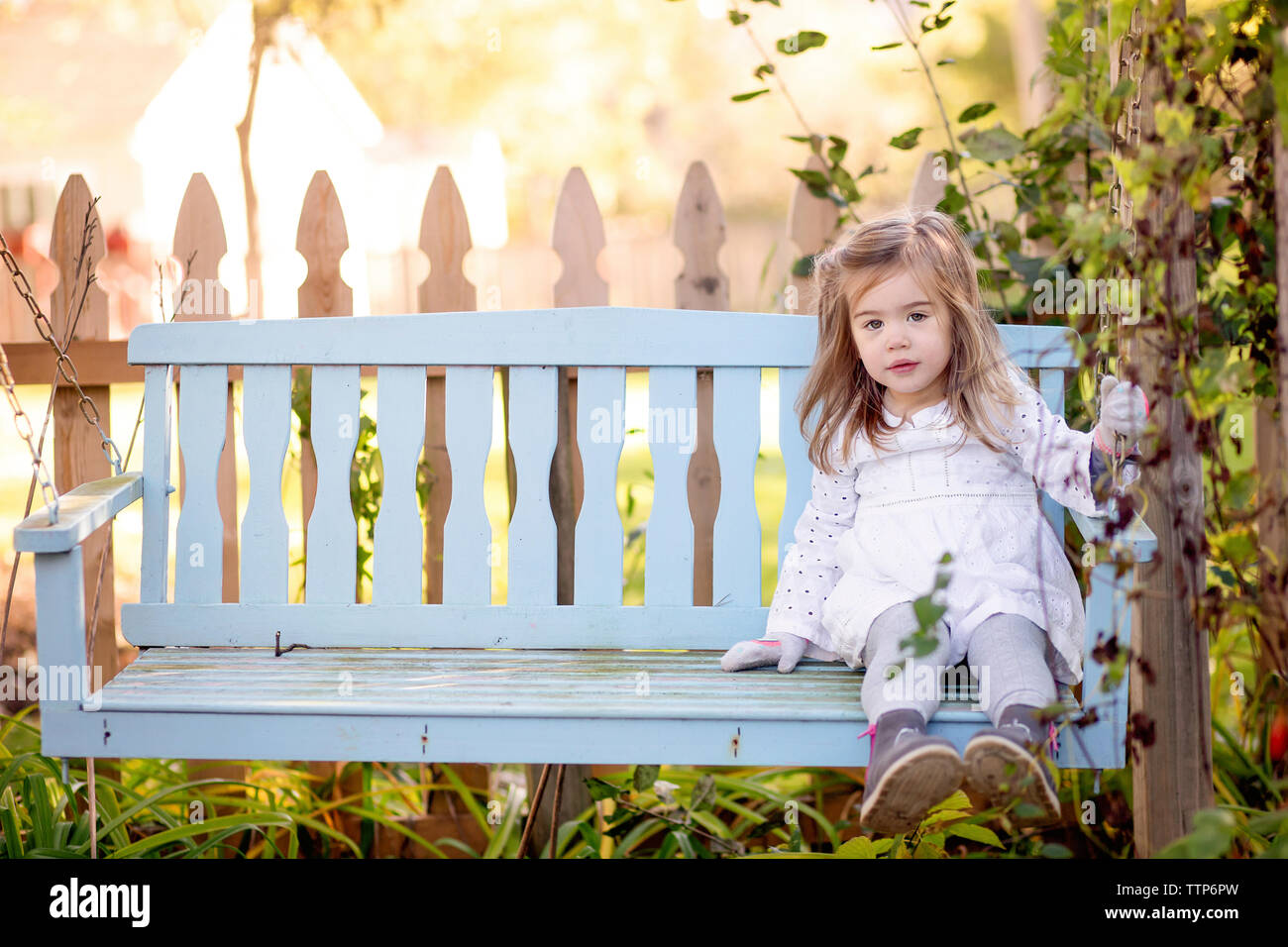 Portrait of cute girl sitting on wooden swing in yard Stock Photo