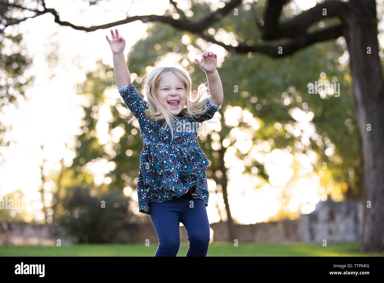 blonde girl jumping with arms in air outside and smiling big Stock Photo