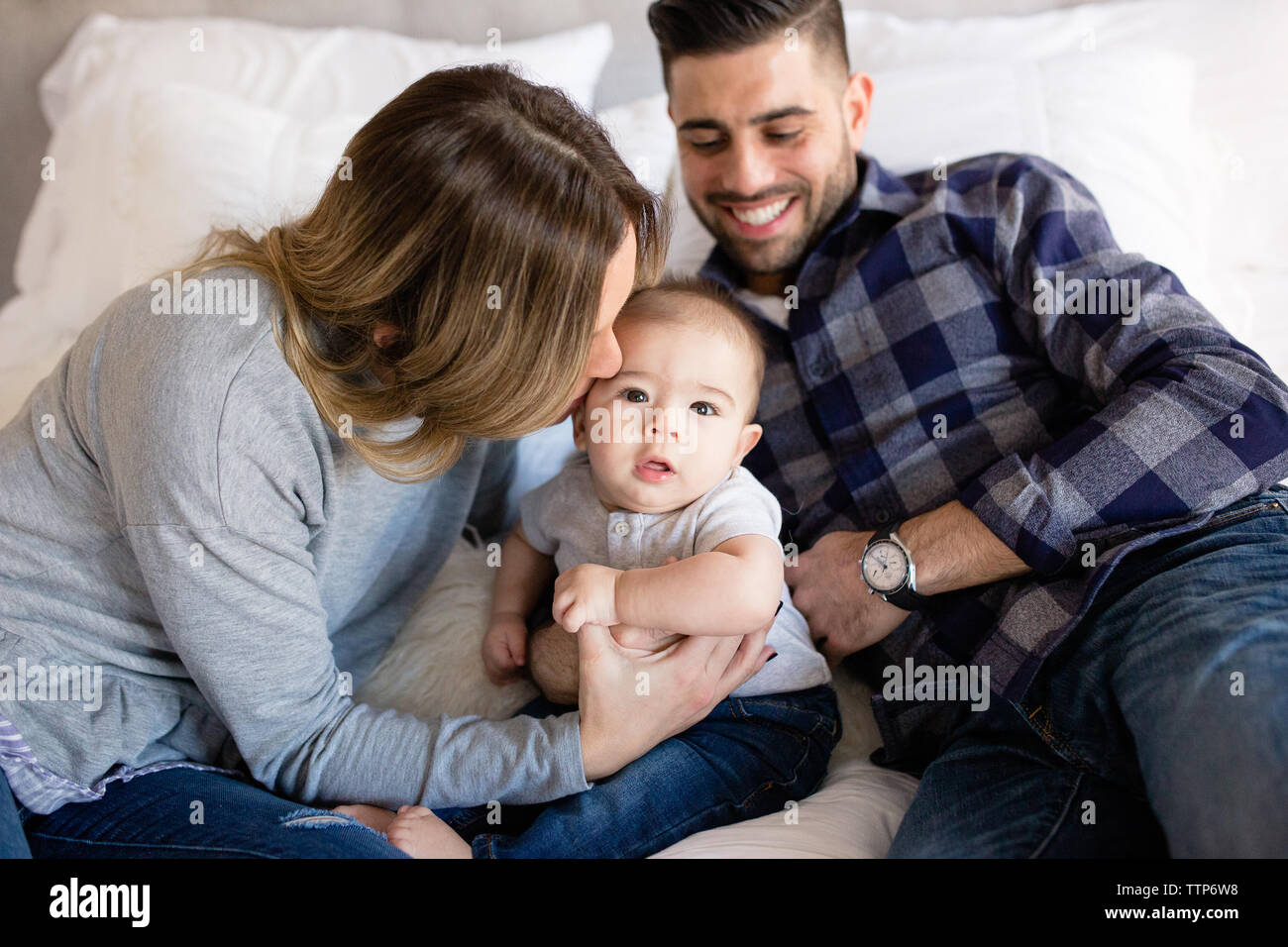 Mom Kissing Cute Baby On Cheek With Dad Smiling In Background Stock Photo Alamy