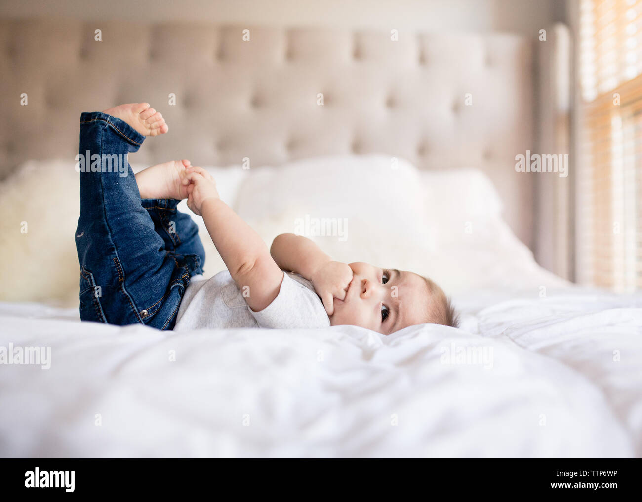 Cute baby boy laying on bed grabbing toes and hand in mouth Stock Photo