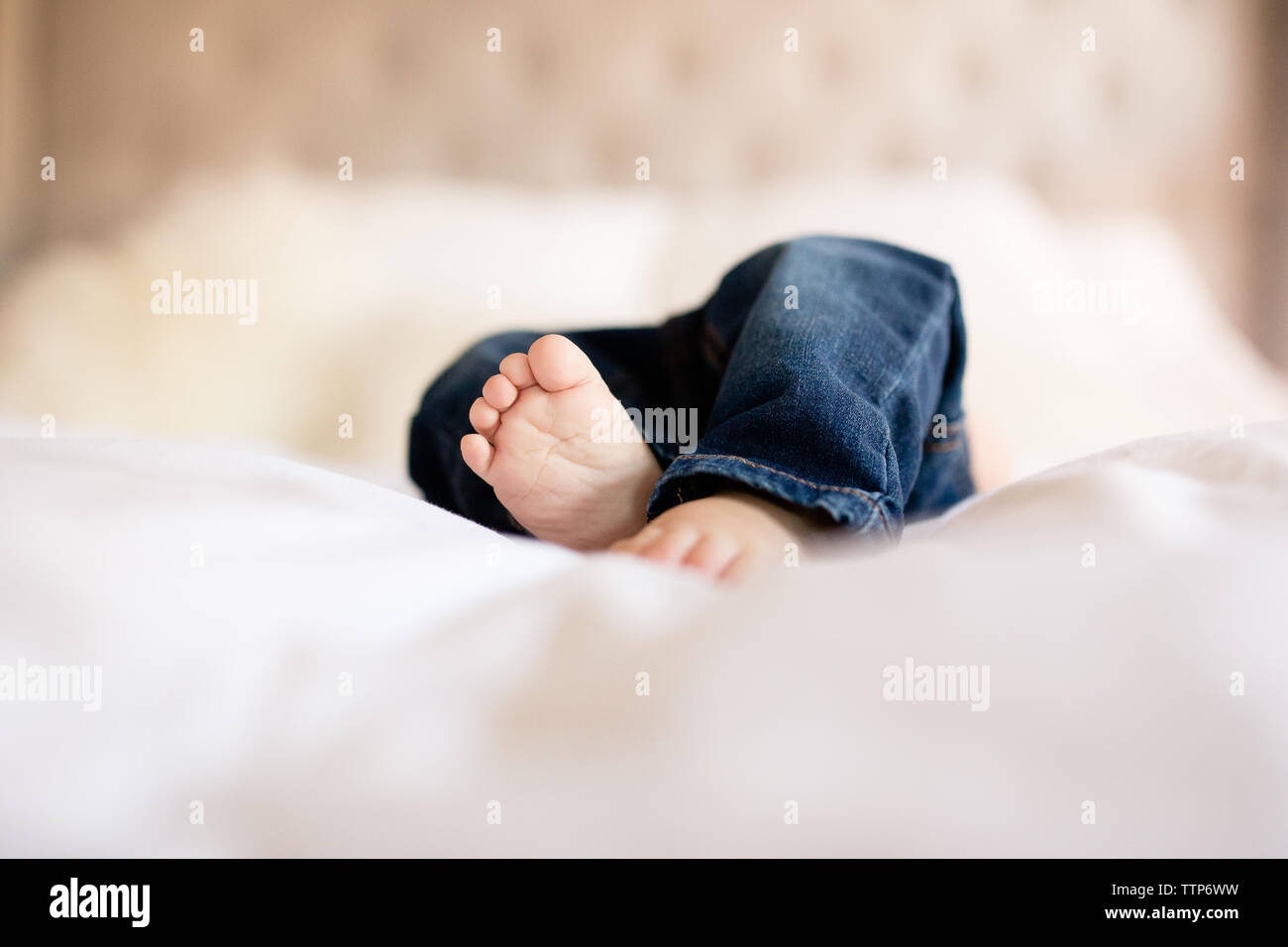 Baby toes peeking out from denim jeans on bed indoors Stock Photo