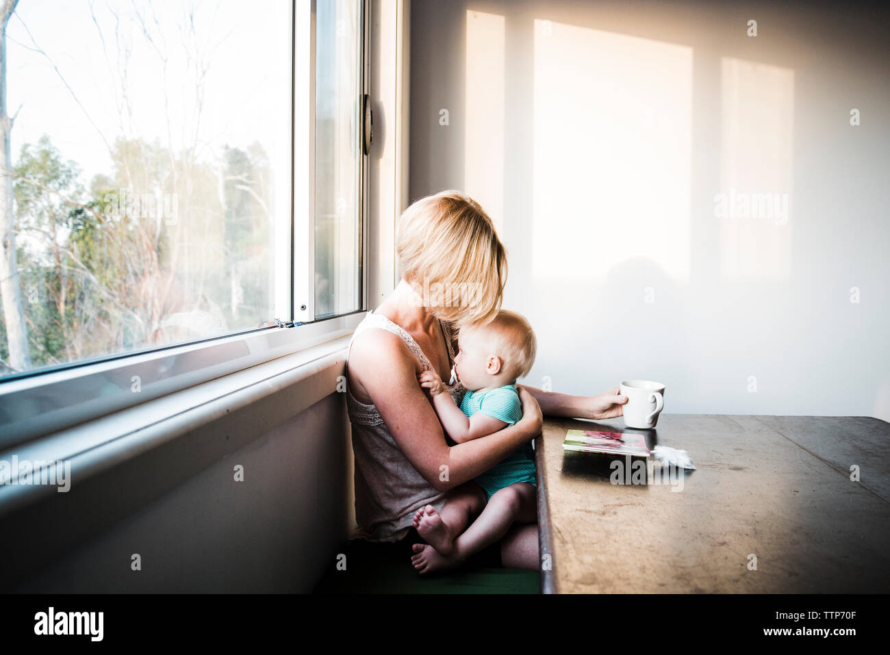 Daughter sucking pacifier while sitting on mother's laps against window at  home Stock Photo - Alamy