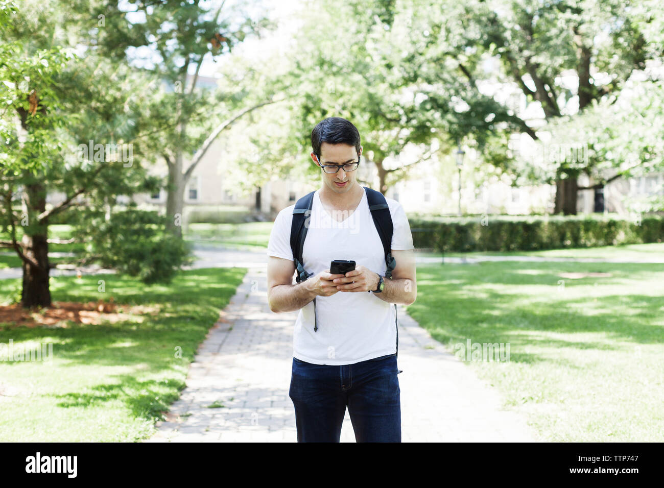 Confident man using mobile phone while standing on footpath at park Stock Photo