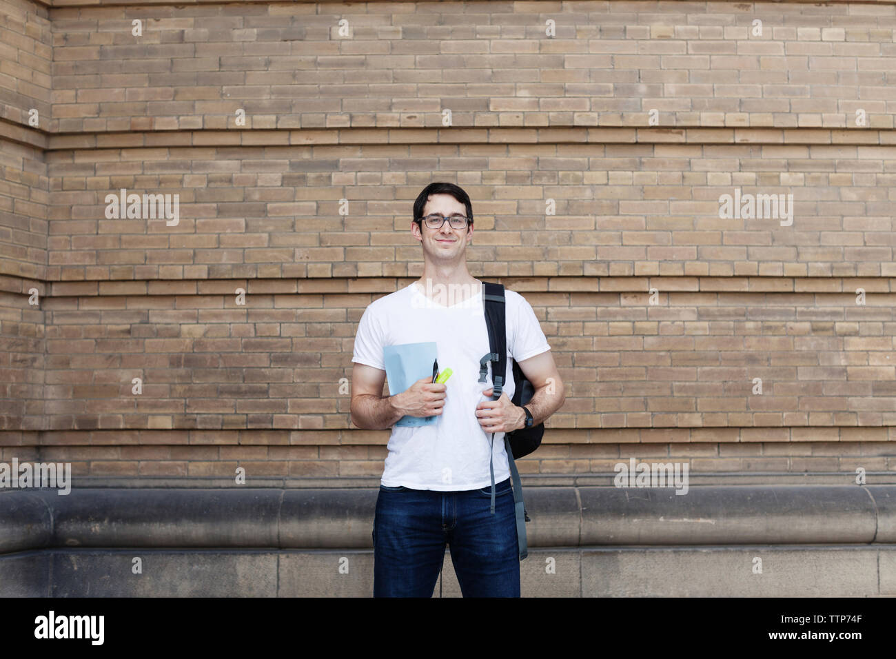 Portrait of smiling male student with backpack standing against brick ...