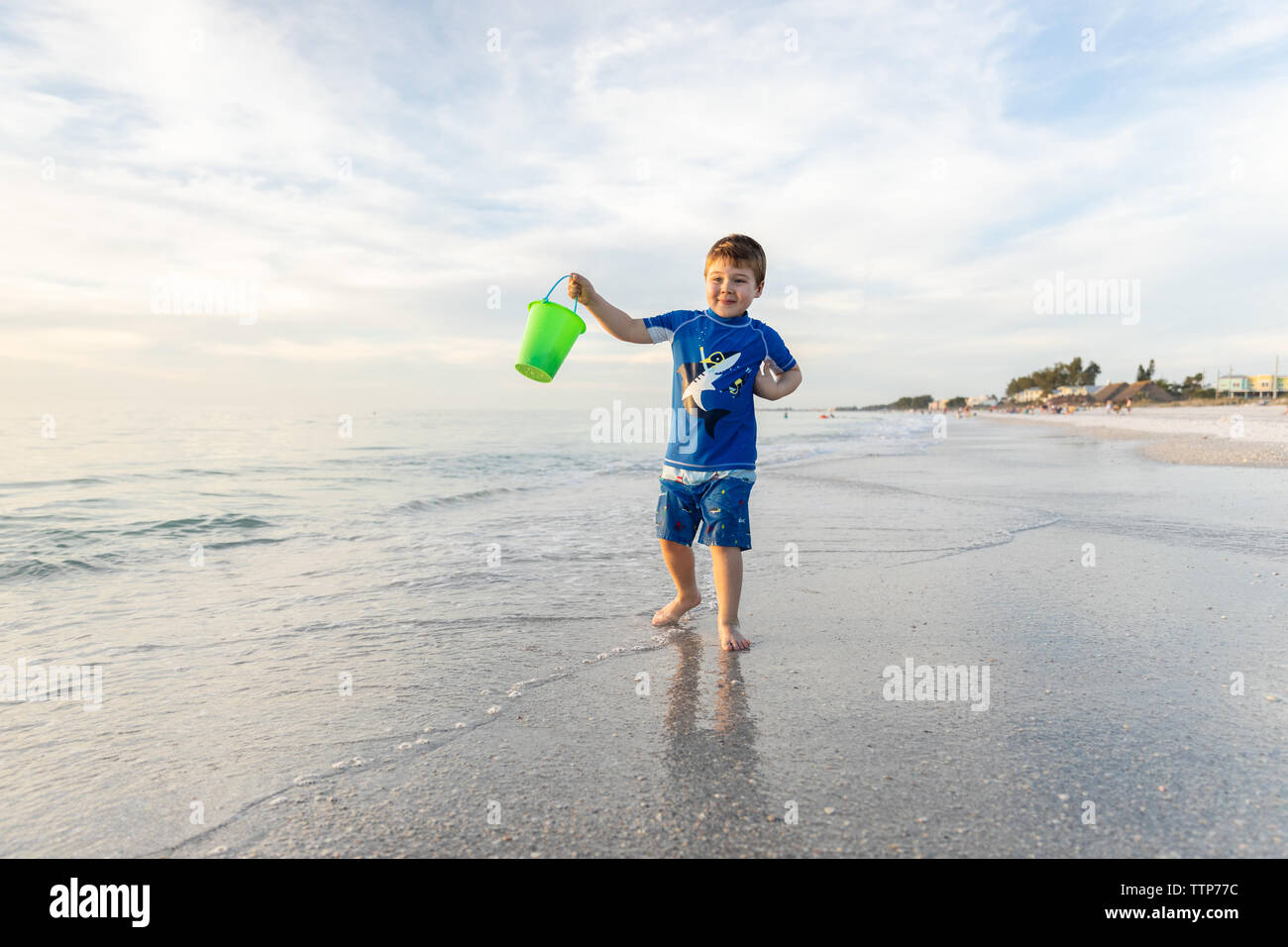 Happy Child With Bucket Walking in the Water at the Beach Stock Photo