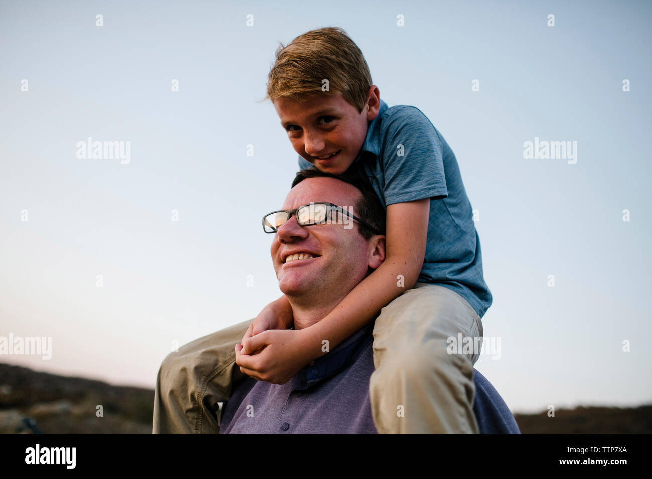 Smiling father carrying son on shoulders against clear sky during sunset Stock Photo