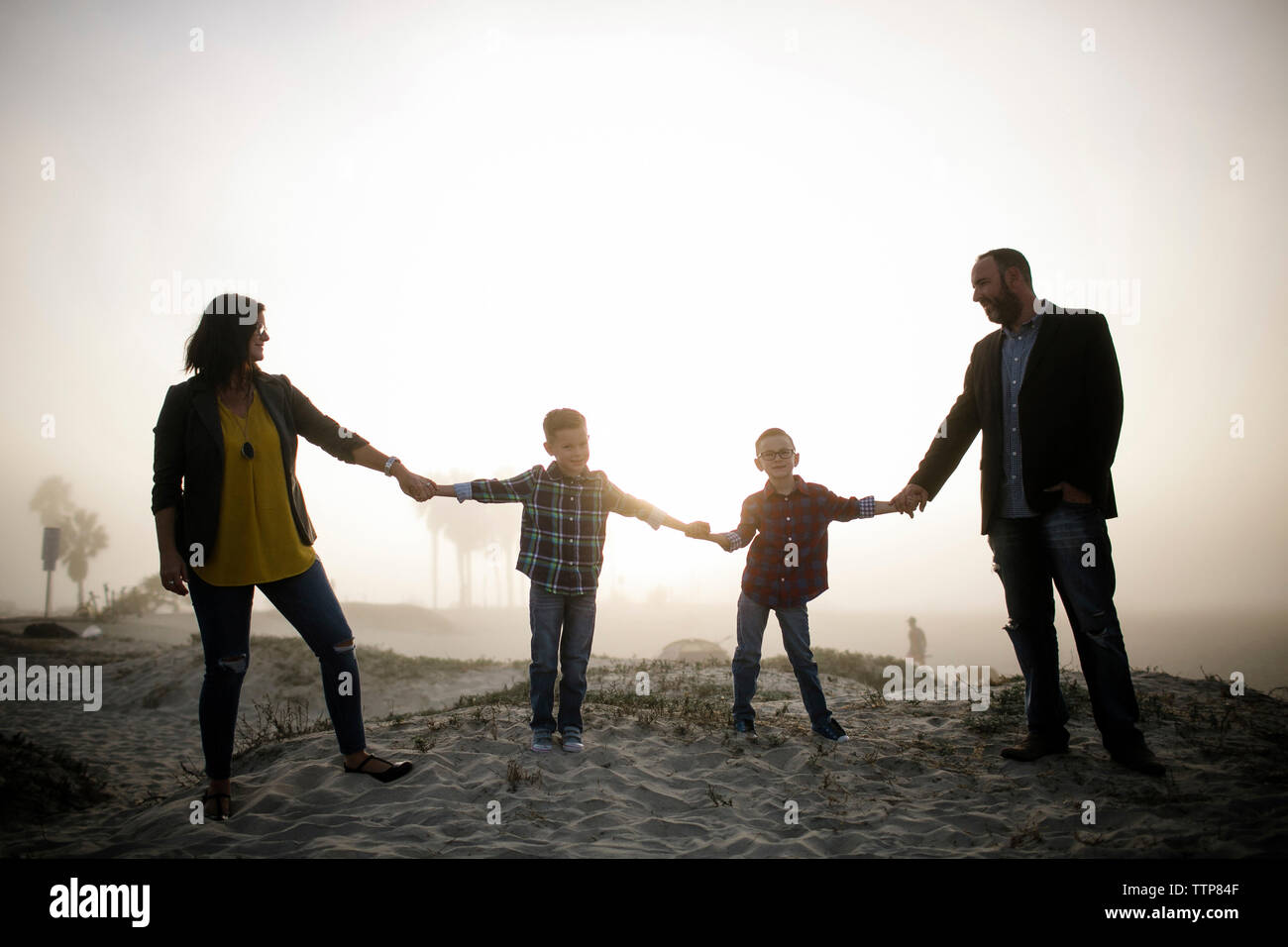 Happy silhouette family holding hands while standing at beach against sky during foggy weather Stock Photo