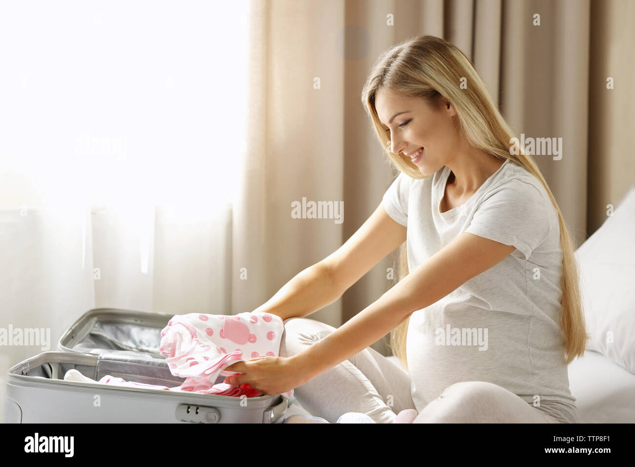 Pregnant woman packing suitcase for maternity hospital at home Stock