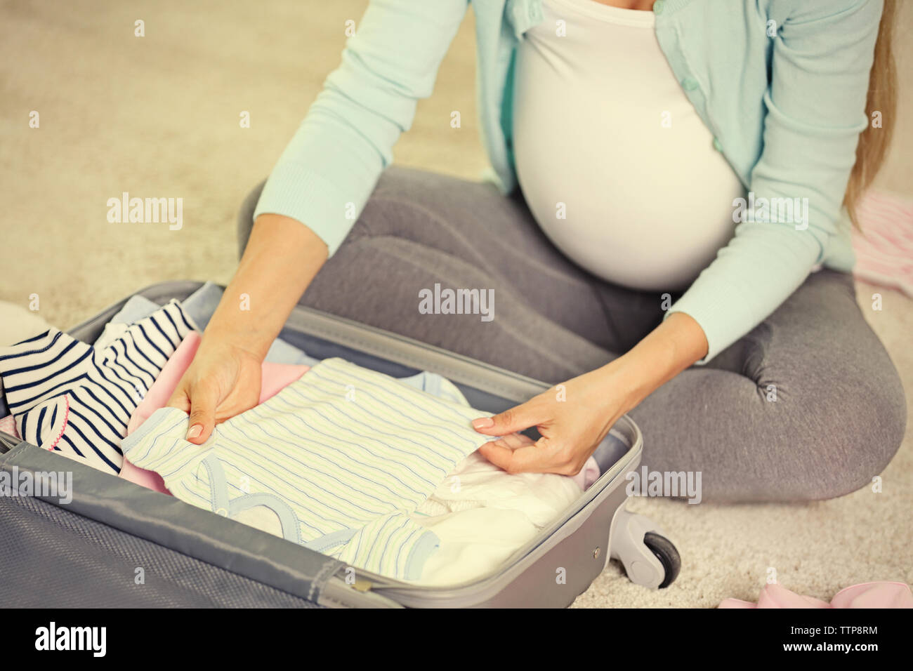 Pregnant woman packing suitcase for maternity hospital at home Stock