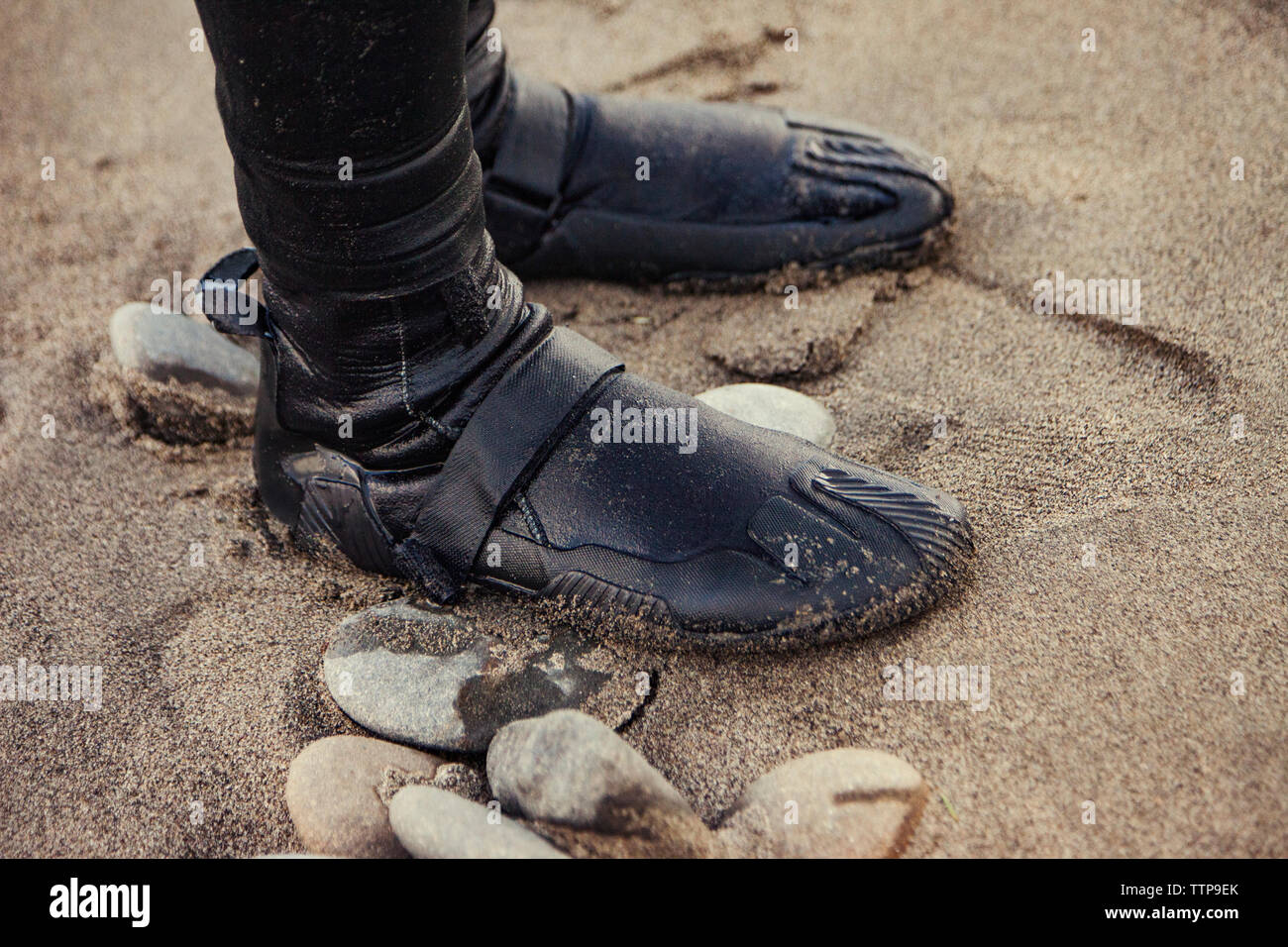 Low section of person wearing wet shoes and standing on sand Stock