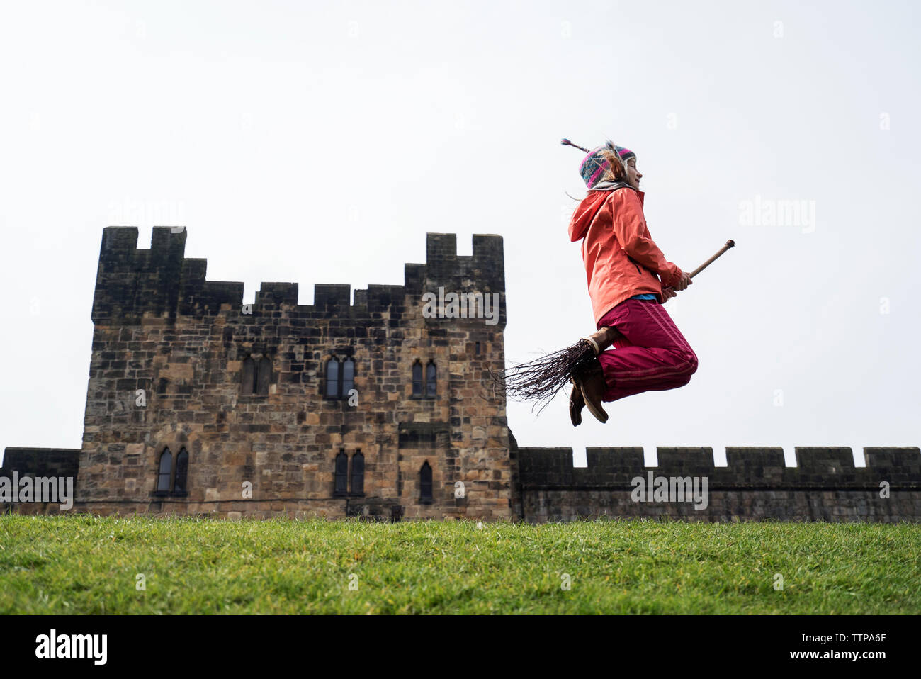 Side view of girl jumping with broom against castle Stock Photo