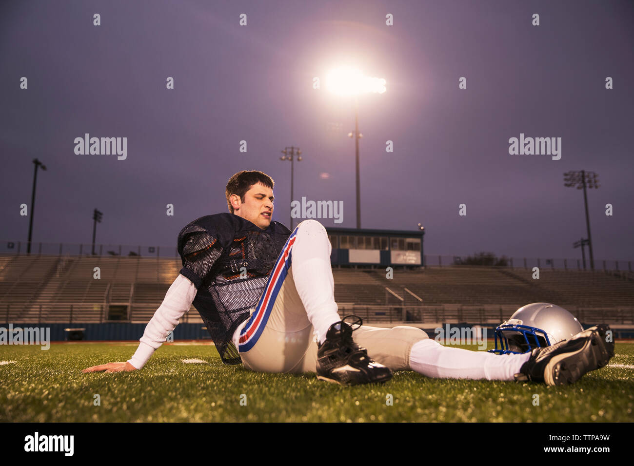 American football player relaxing on grassy field at stadium against sky Stock Photo